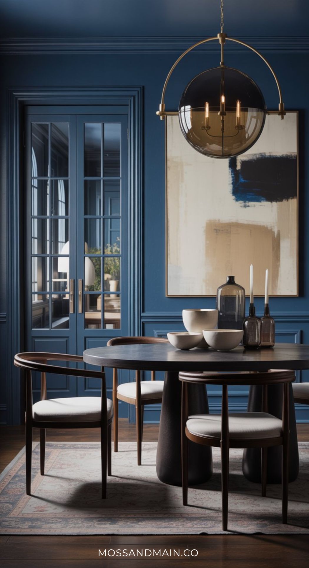 A modern dark blue dining room with navy walls, a round black table, four wooden chairs with white seats, a large abstract painting, decorative bowls, candles, and a glass pendant light overhead.