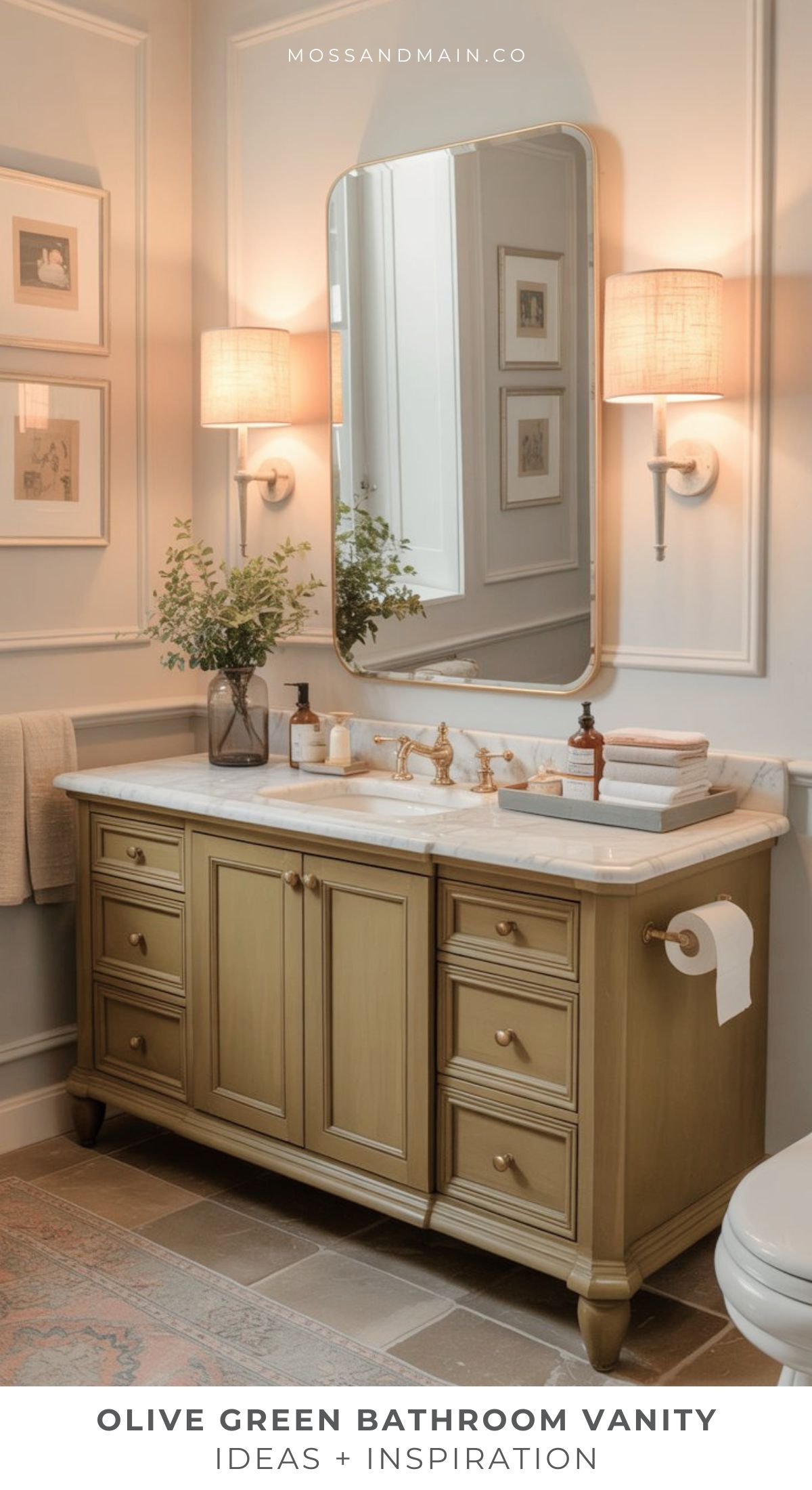 A bathroom vanity in olive green with a white countertop, gold hardware, and decorative items like a vase, soap, and towel. A large mirror and two wall sconces are above the vanity, framed by elegant wall decor.