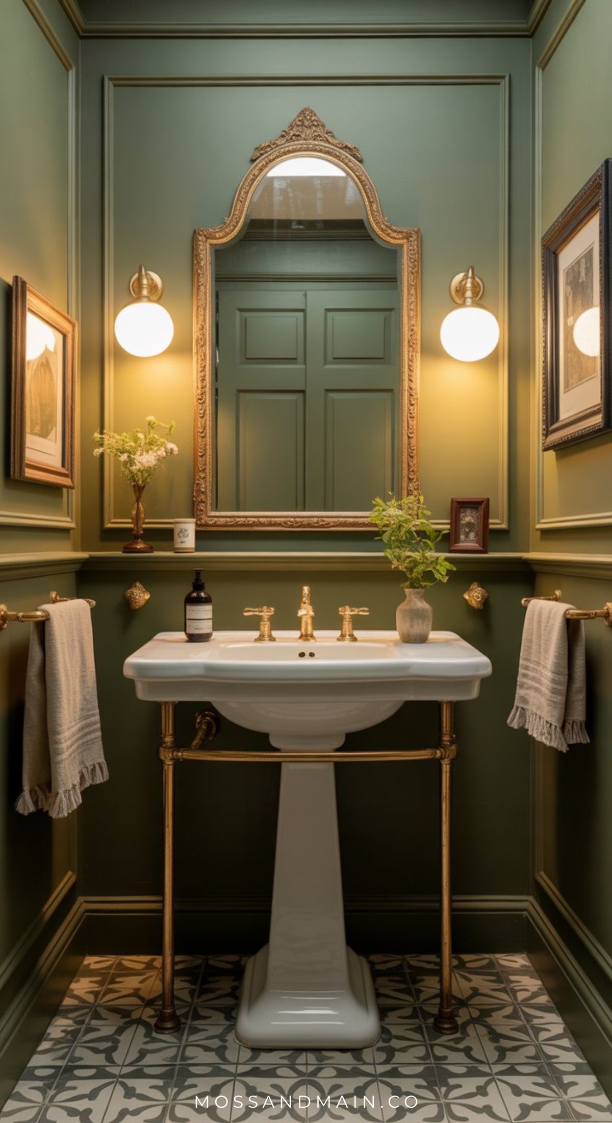 Elegant Olive Green Bathroom with paneled walls, a white pedestal sink and gold fixtures, ornate mirror, globe sconces, framed art, and patterned floor tiles. Towels hang on gold bars—perfect inspiration for chic Bathroom Designs.