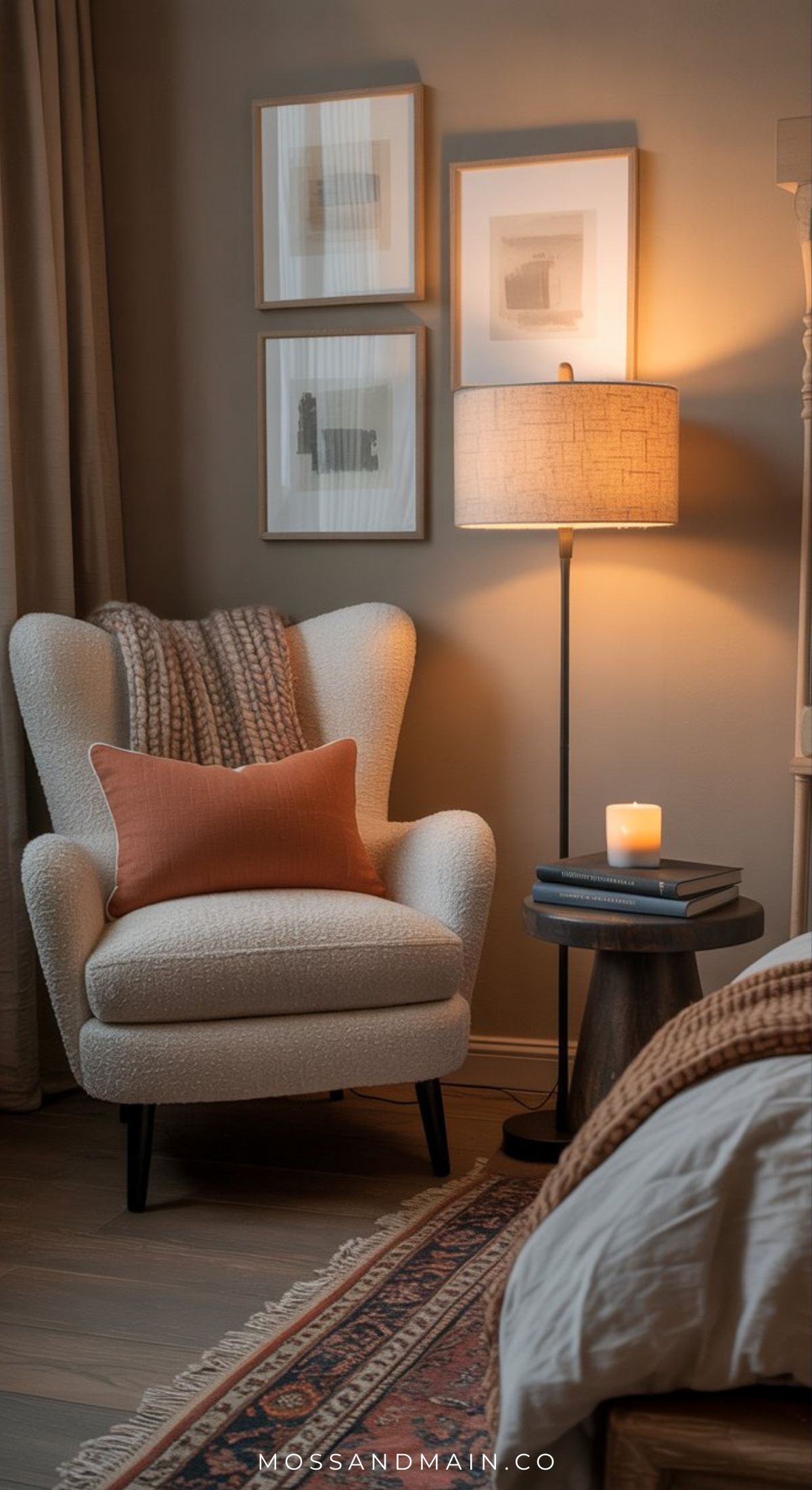 A cozy escape awaits in this reading nook, featuring a cream armchair, brown throw, and orange pillow beside a round side table, softly illuminated by a floor lamp and candle. Three framed art pieces adorn the beige wall above.