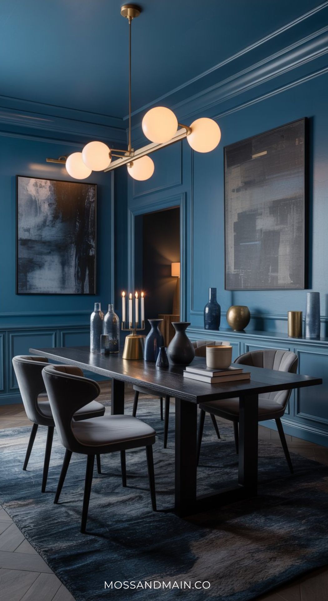 A modern dark blue dining room with abstract art, a dark wood table, white cushioned chairs, decorative vases, lit candles, and a gold chandelier with round bulbs. The room exudes a stylish, contemporary feel.